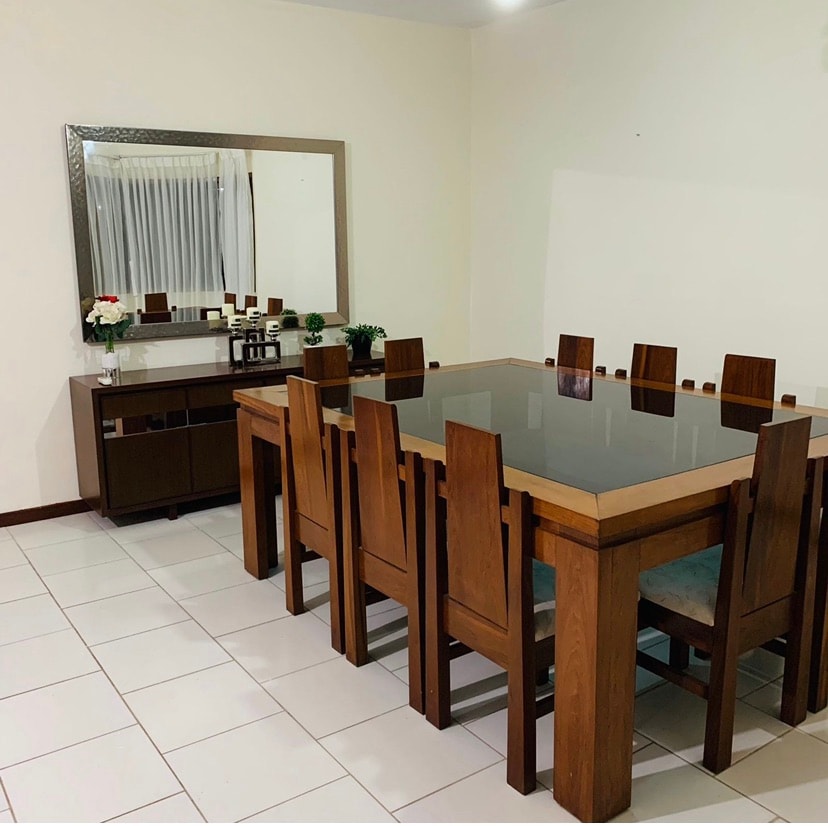 A dining area is furnished with a large, rectangular table surrounded by ten wooden chairs. A mirror with a metallic frame hangs on the wall, reflecting the natural light from the adjacent window. A sideboard offers additional storage and decorative touches.