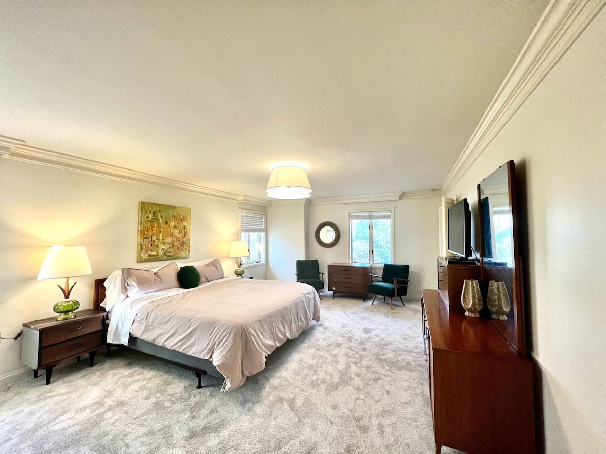 Master Bedroom, featuring a king-sized bed, an attached master bathroom, a large TV and a lounge area.