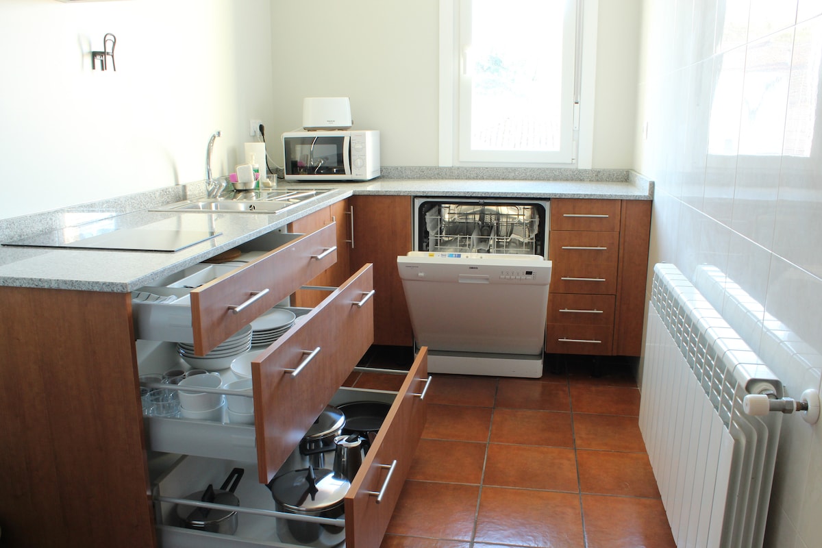 A modern kitchen features wooden cabinets with multiple drawers, showcasing organized dishware and cookware. Stainless steel appliances, including a microwave and dishwasher, are visible. A neutral color palette enhances the space, complemented by a window allowing natural light to illuminate the countertop.