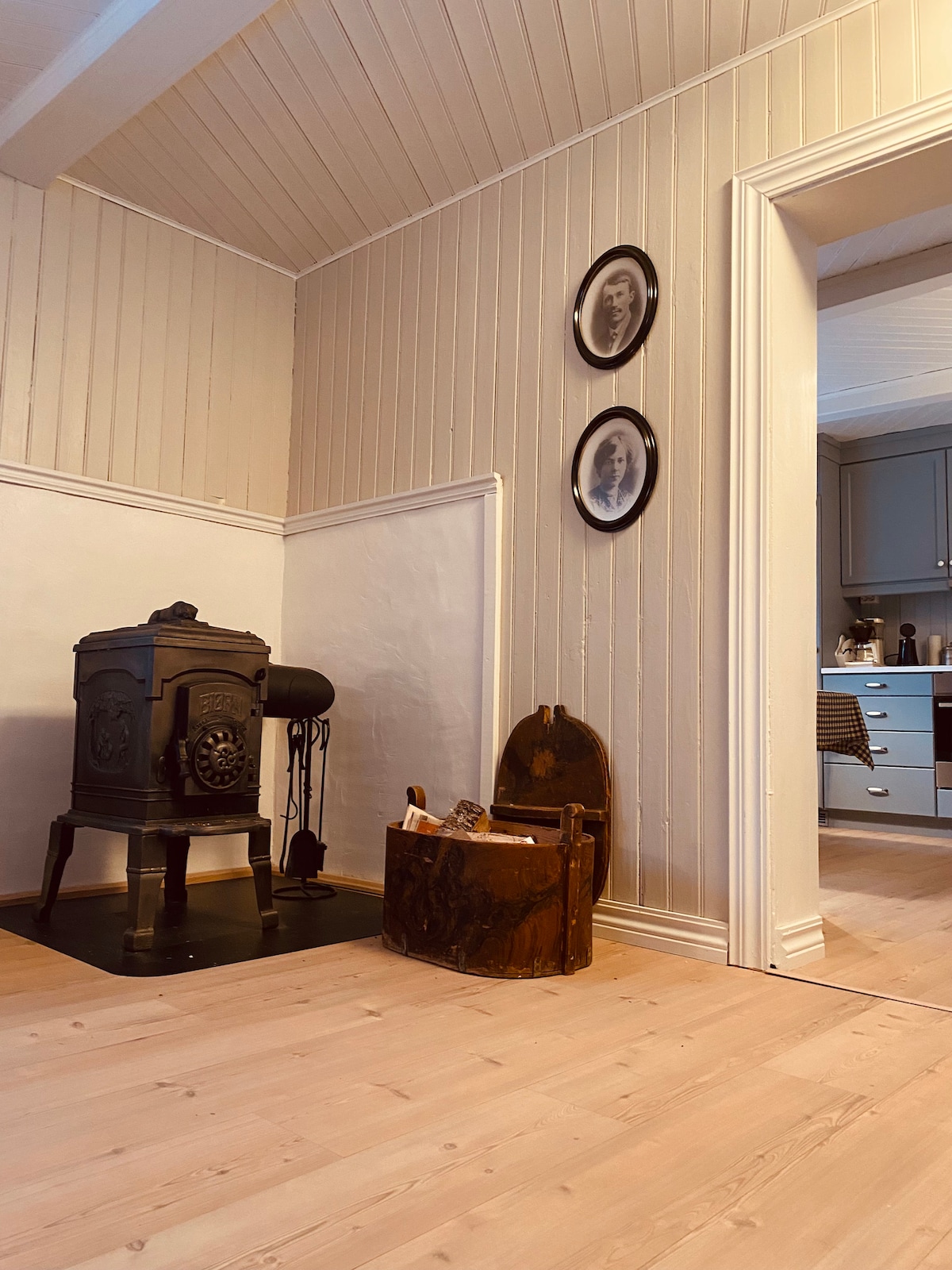 A charming interior space features a traditional wood stove positioned against a rustic wall, enhancing the room's warmth. Two black-framed circular wall plates add a decorative touch above. A wooden crate and a vintage item sit on the floor, contributing to the inviting atmosphere.