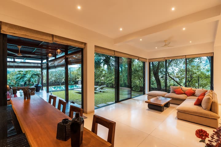 ✨Expansive living room with floor-to-ceiling glass walls, warm-toned decor, and seamless views of the garden, pool and wooden cabana: perfect for indoor-outdoor living✨