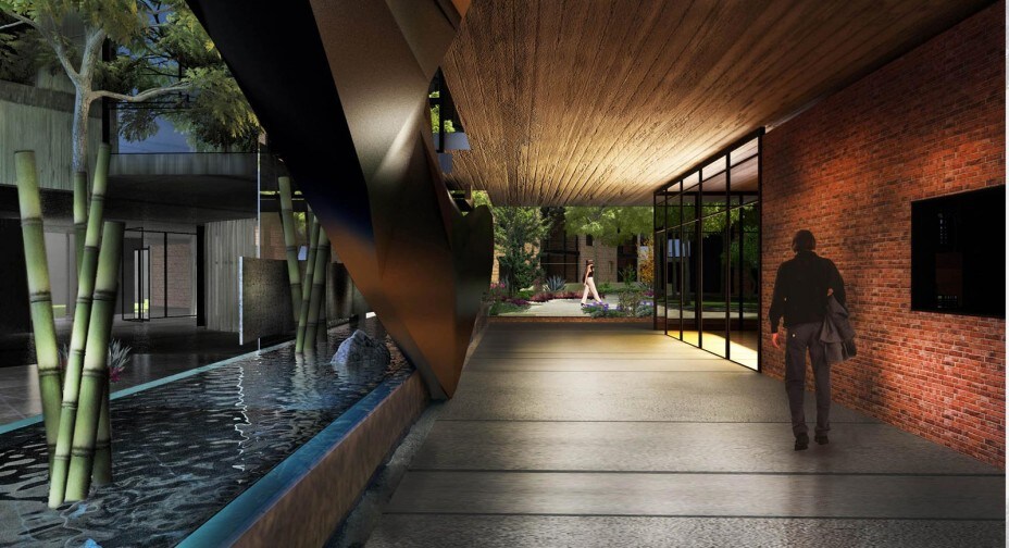An inviting entrance area features a combination of brick and metal design, with a water feature running alongside. Lush greenery is visible through large glass windows, while an individual walks along the spacious pathway, surrounded by modern architectural elements.