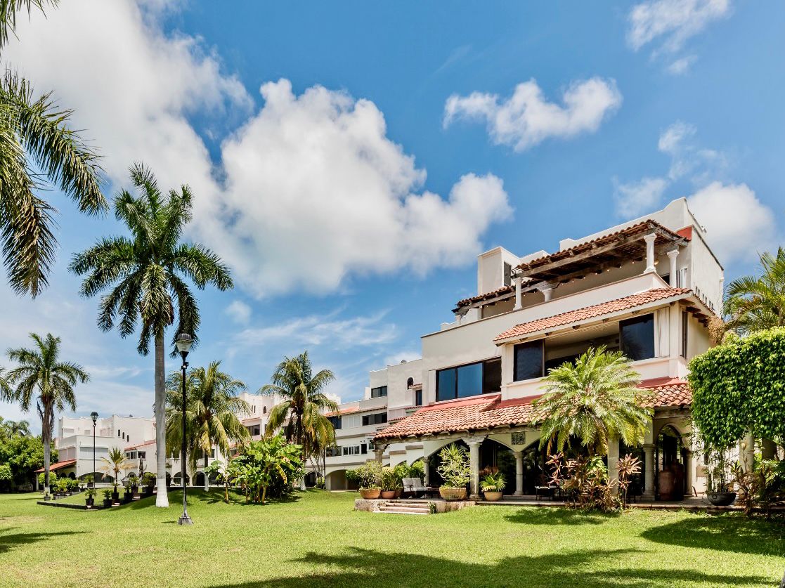The villa is situated within a residential complex, surrounded by lush greenery and palm trees. The building showcases traditional tiles and large windows, while open spaces invite relaxation in a serene environment.