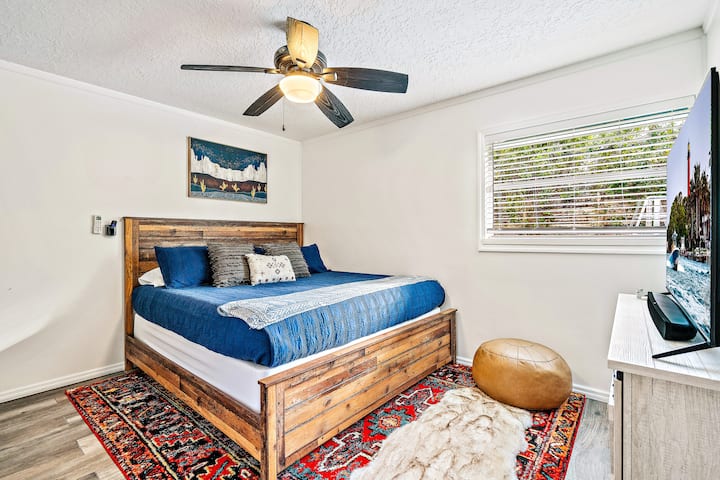 غرفة النوم 1 - سرير بحجم كبير ومرتبة أرجوانية وتلفزيون روكو بمقاس 55 بوصة مزود بشريط صوت وخزانة ملابس مفتوحة ومكتب مزود بمرآة ومرآة مكياج ومجفف شعر مثبت على الحائط في الزاوية. 