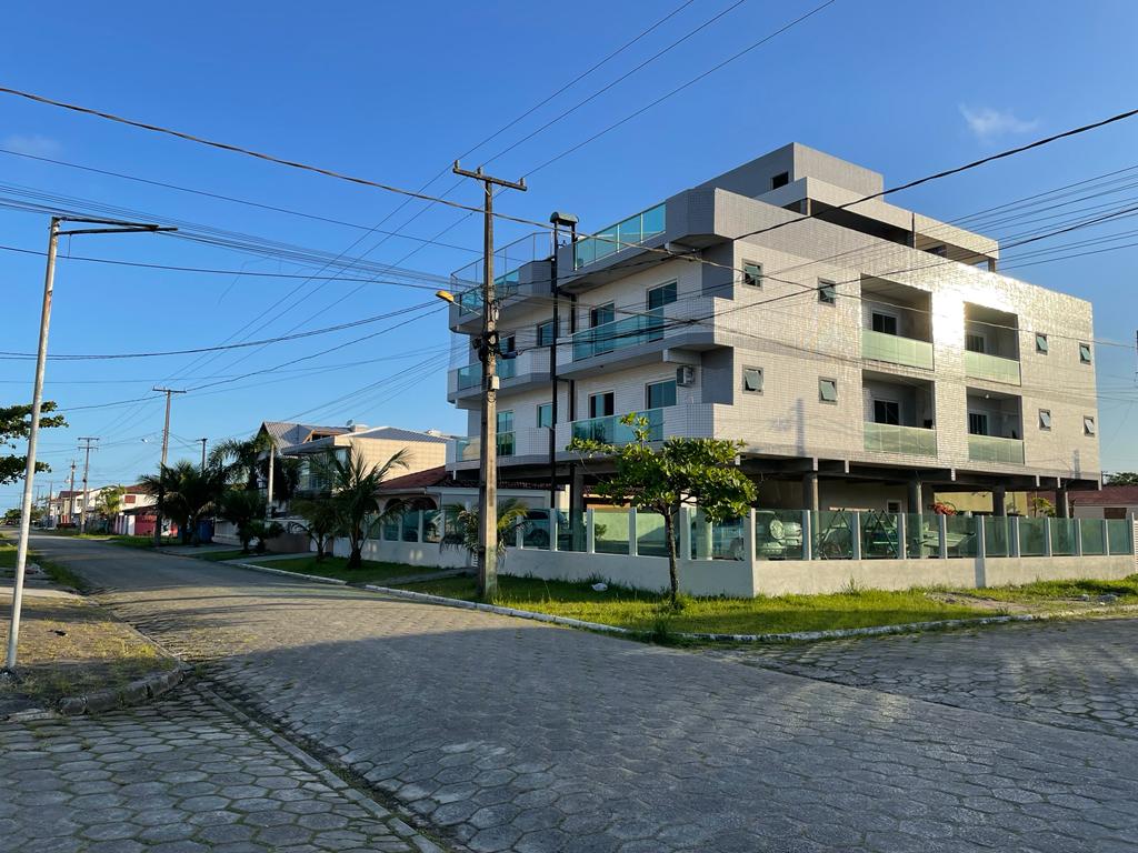 A modern multi-story building is situated at the end of a quiet street, featuring balconies and large windows. The façade is designed with light-colored materials, while the surrounding area includes greenery and paved sidewalks leading up to the property.