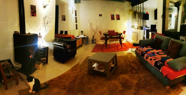 A spacious living and dining area features a mix of seating options including a comfortable sofa and an armchair. A dining table is set for gatherings, and warm lighting enhances the inviting atmosphere. The floor is accented with a large area rug, while a decorative fireplace adds charm.