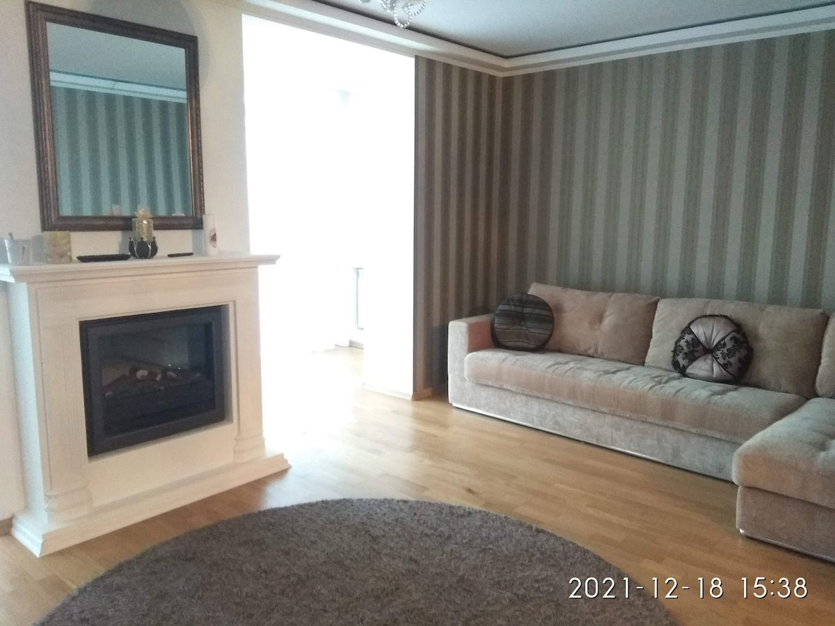 A modern living area features a plush, neutral-colored sofa against a striped wall, paired with a circular area rug. A sleek fireplace provides warmth, while a large mirror reflects light, enhancing the spaciousness of the room.