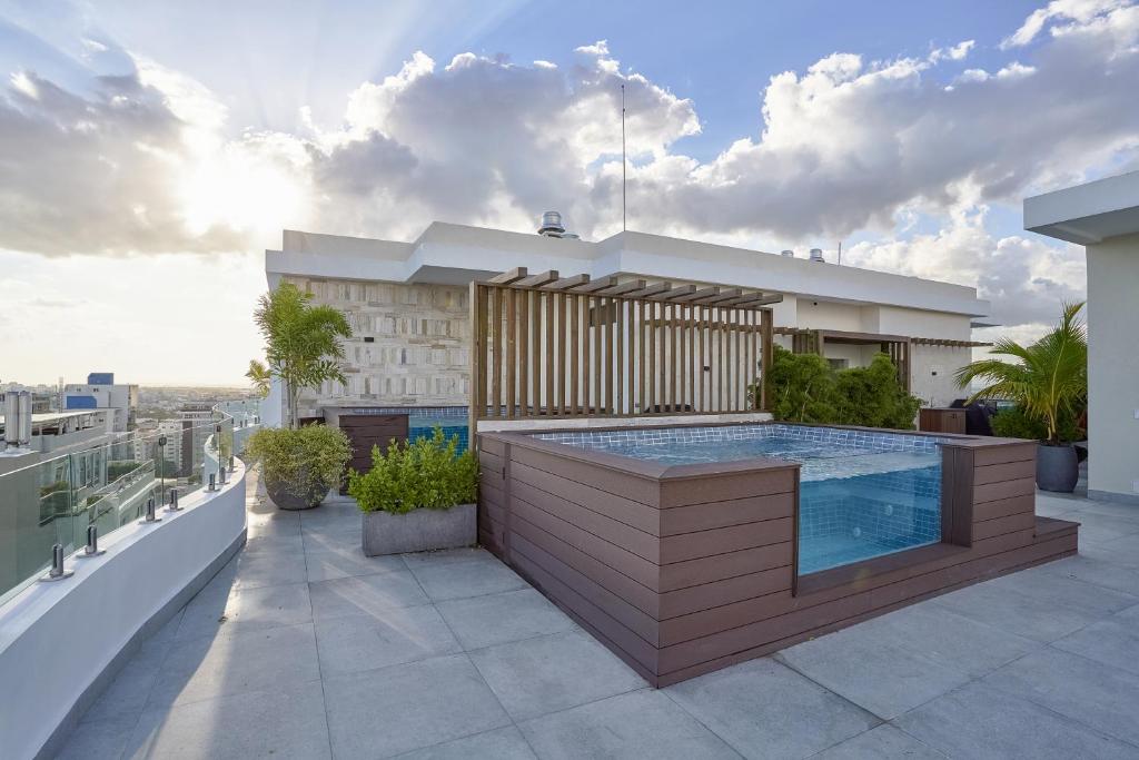A private jacuzzi sits on a spacious rooftop area, surrounded by modern wooden decking and lush greenery. The sunset casts a warm glow, highlighting the refreshing water and inviting ambiance of the outdoor space.