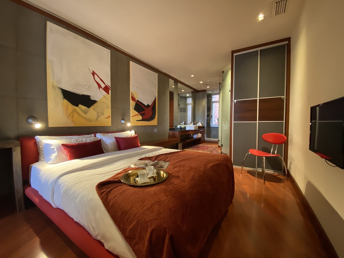 מיטה זוגית גדולה עם טלוויזיה חכמה התלויה על הקיר ושפע של מקום תלייה וחדרי רחצה צמודים. 