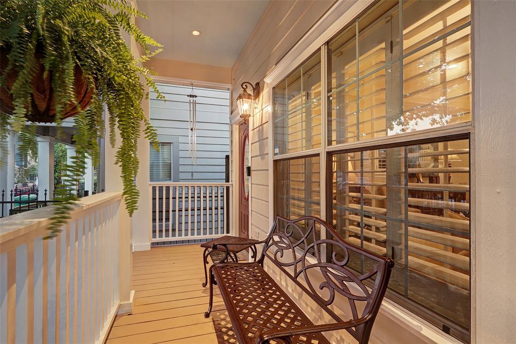 A welcoming porch area features a decorative bench surrounded by lush ferns. Light streaming through the glass windows highlights the classic wood design. The layout allows easy access to outdoor spaces while providing a cozy spot to relax.
