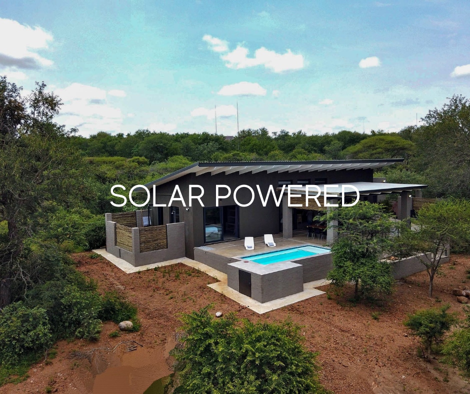 An aerial view showcases a modern home surrounded by lush greenery, featuring a small swimming pool and outdoor seating area. The use of solar panels is indicated, emphasizing the commitment to sustainability. A spacious outdoor area blends seamlessly with the natural landscape.