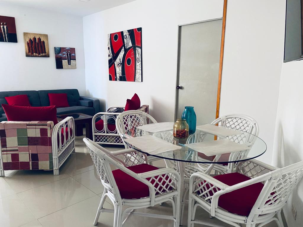 A modern living area is featured, showcasing a glass dining table surrounded by six chairs. A comfortable gray sofa is positioned against the wall, complemented by accent pillows. Colorful wall art adds visual interest to the space, enhancing the overall decor.