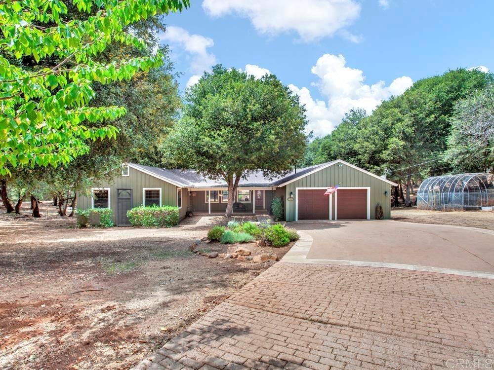 The exterior of the cabin is showcased, featuring a green facade with a welcoming porch. Lush trees surround the property, providing shade and a natural ambiance. A spacious driveway leads up to the home, enhancing accessibility and inviting guests to explore the serene setting.