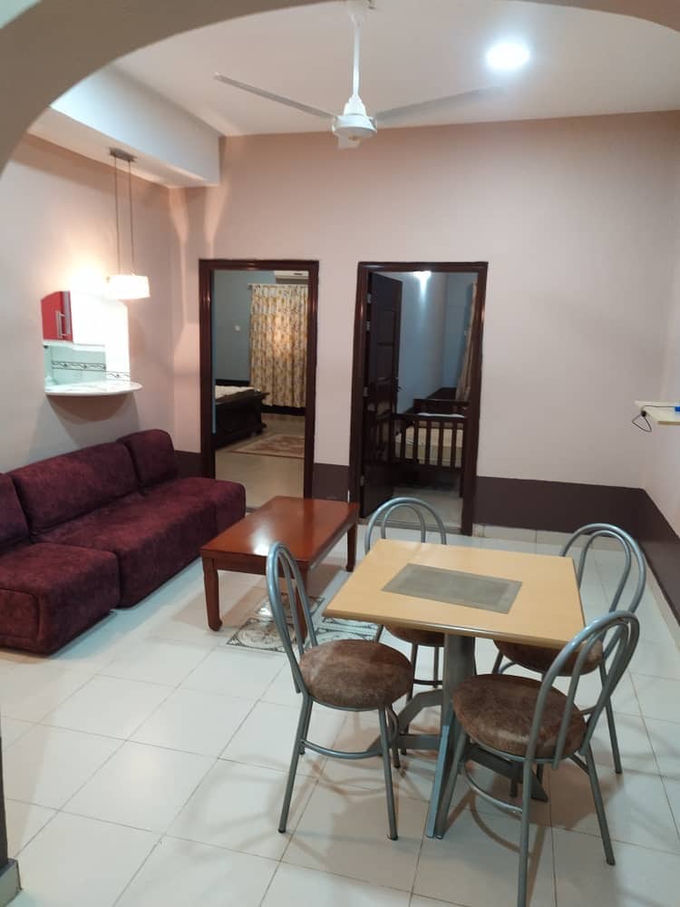 A cozy seating area is presented with a maroon sofa, complemented by a wooden coffee table. A small dining table with metal chairs occupies the adjacent space. Doorways lead to other rooms, and soft lighting is provided by overhead fixtures.