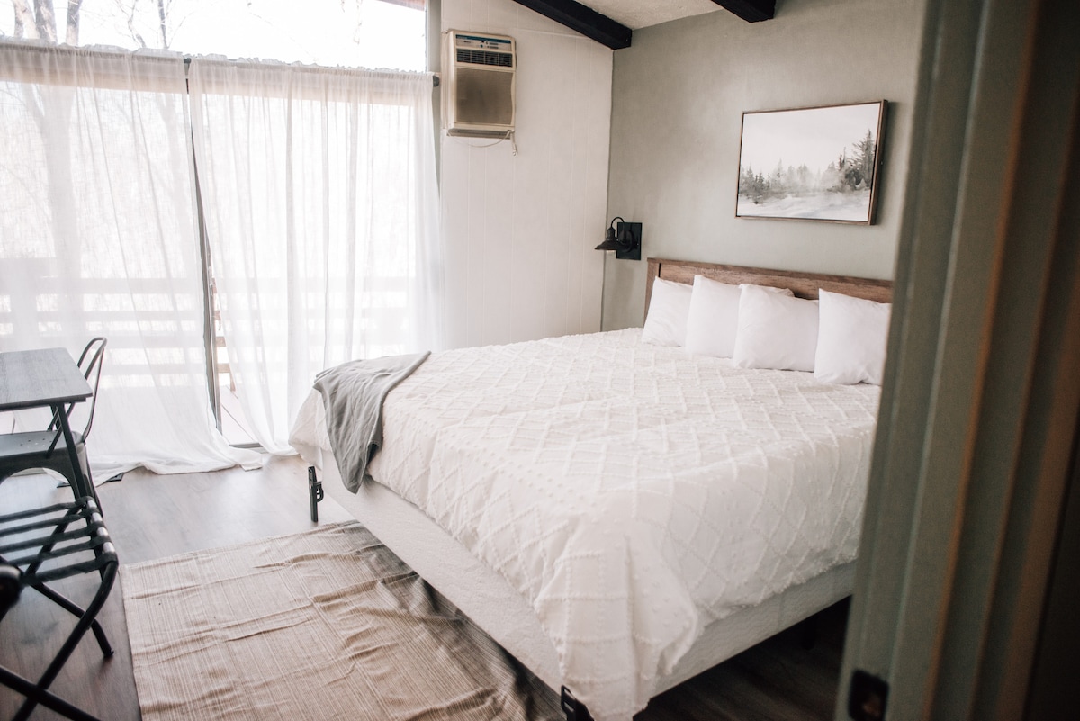 Main level King bedroom.  Featuring vaulted ceilings with exposed beams.  Sliding door access to the deck. 

Note: the house was recently renovated to add central air and the a/c unit pictured is no longer necessary.