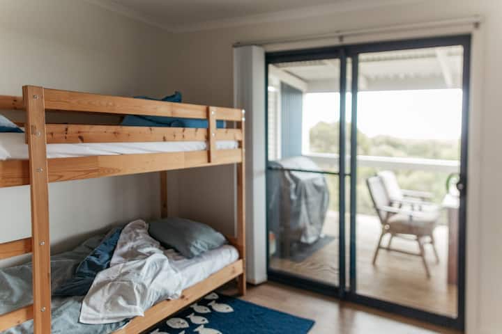 The third bedroom includes one single bunk-bed, a dresser and a large pedestal fan.  There is a lockable sliding door, with access to the rear deck.