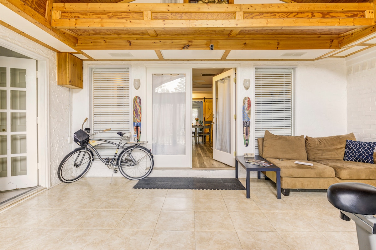 A spacious foyer showcases a comfortable seating area with a sofa and coffee table. Natural light filters through large glass doors leading to the outdoor area. A bicycle is parked next to the entrance, while textured tiles cover the floor, enhancing the welcoming environment.