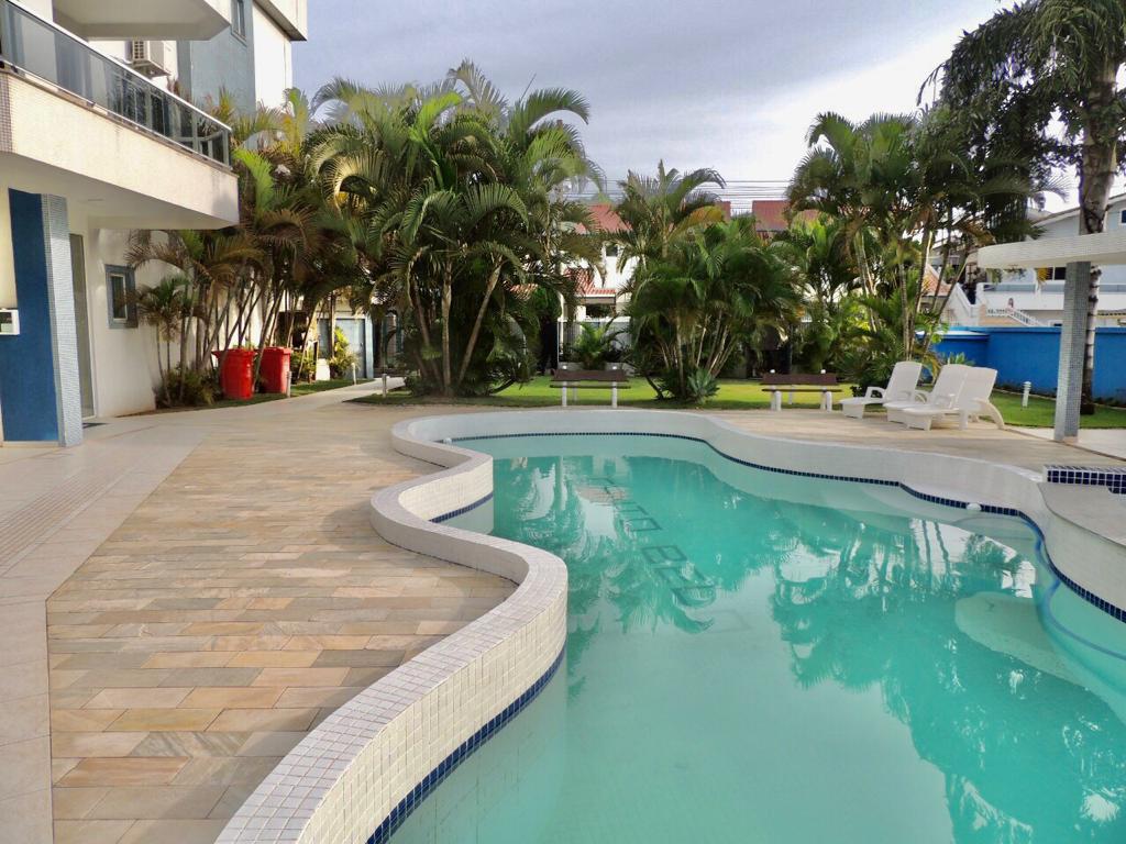The swimming pool is surrounded by lush greenery, featuring lounge chairs and shaded areas for relaxation. The pool is clean and inviting, reflecting the surrounding palm trees and landscaping in its calm waters.