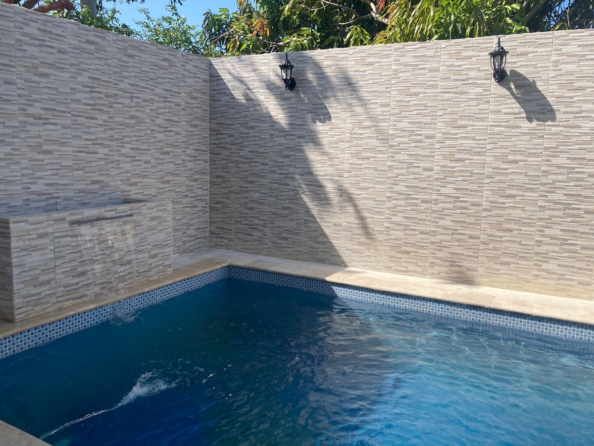 A private pool is surrounded by textured stone walls, with light casting gentle shadows across the water's surface. Two wall-mounted lanterns provide subtle lighting, enhancing the peaceful ambiance of the outdoor space.