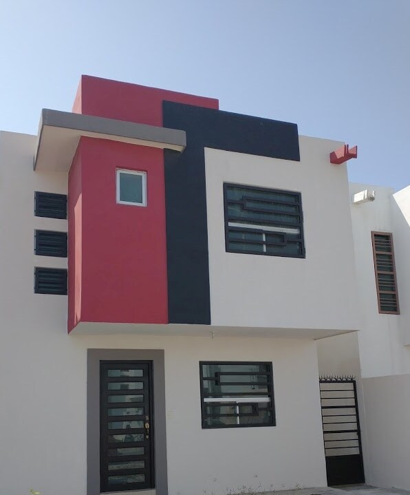 The exterior of the house features a modern architectural design with a combination of white walls and bold accents in red and black. Large windows are framed in dark materials, providing ample natural light and a contemporary appearance. A secure entrance is visible at the front.