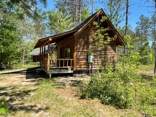 The cabin, constructed from logs, features a welcoming porch with a rail, surrounded by a natural landscape with greenery and trees. The rustic exterior blends harmoniously with its tranquil woodland setting, showcasing the peaceful atmosphere of the north woods.