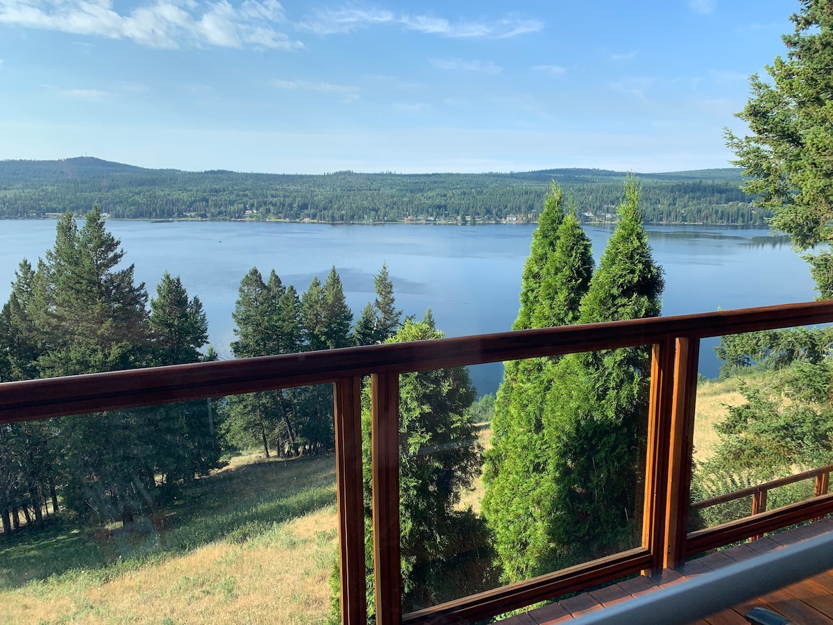 The image captures a scenic view from a balcony overlooking Horse Lake. Lush greenery lines the shore, and gentle waves reflect the clear blue sky. The railing adds a warm wooden touch to the tranquil landscape, inviting guests to enjoy the serene environment.