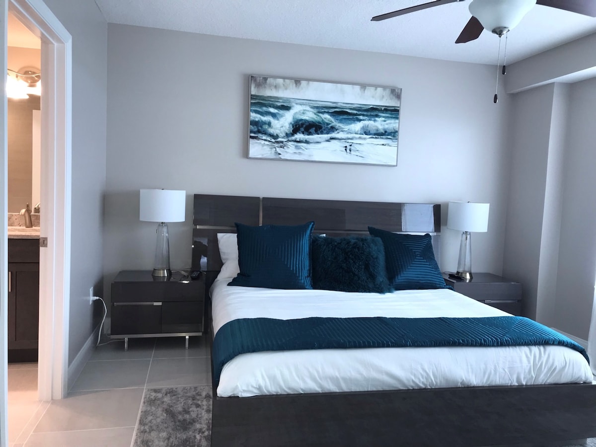 Главна спалня с суперголямо двойно легло, вентилатор на тавана, скрин, пълен гардероб, стол за сядане и 65 - инчов смарт телевизор.