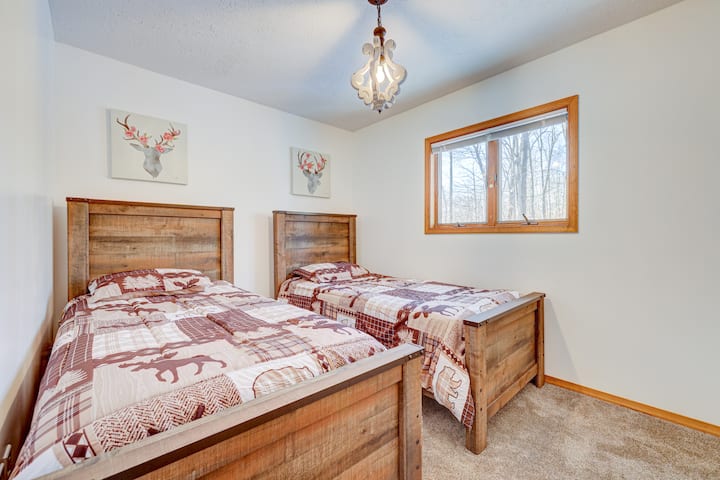 Chambre confortable avec deux lits jumeaux en bois rustique, charmante literie sur le thème de la faune et lumière naturelle qui passe par une grande fenêtre. Parfait pour un séjour paisible et confortable dans un cadre serein.