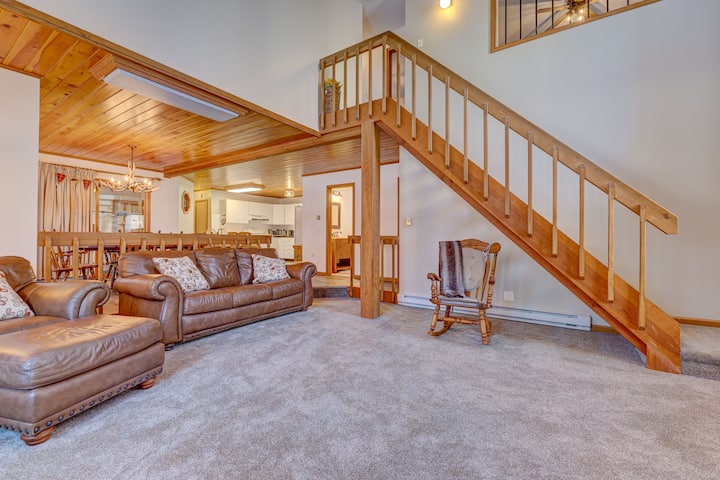 Spacieux salon avec des sièges en cuir moelleux, un plafond en bois chaud et un escalier ouvert. Parfait pour la détente, avec des touches confortables comme un fauteuil à bascule et un flux ouvert vers la salle à manger et la cuisine.