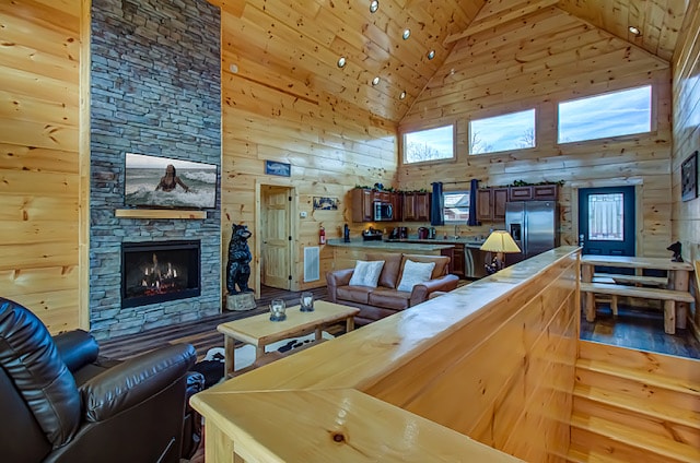 An open living area features a stone fireplace as the focal point, surrounded by large windows allowing natural light to fill the space. Comfortable seating is arranged for relaxation, and the kitchen area can be seen in the background, equipped with modern appliances.