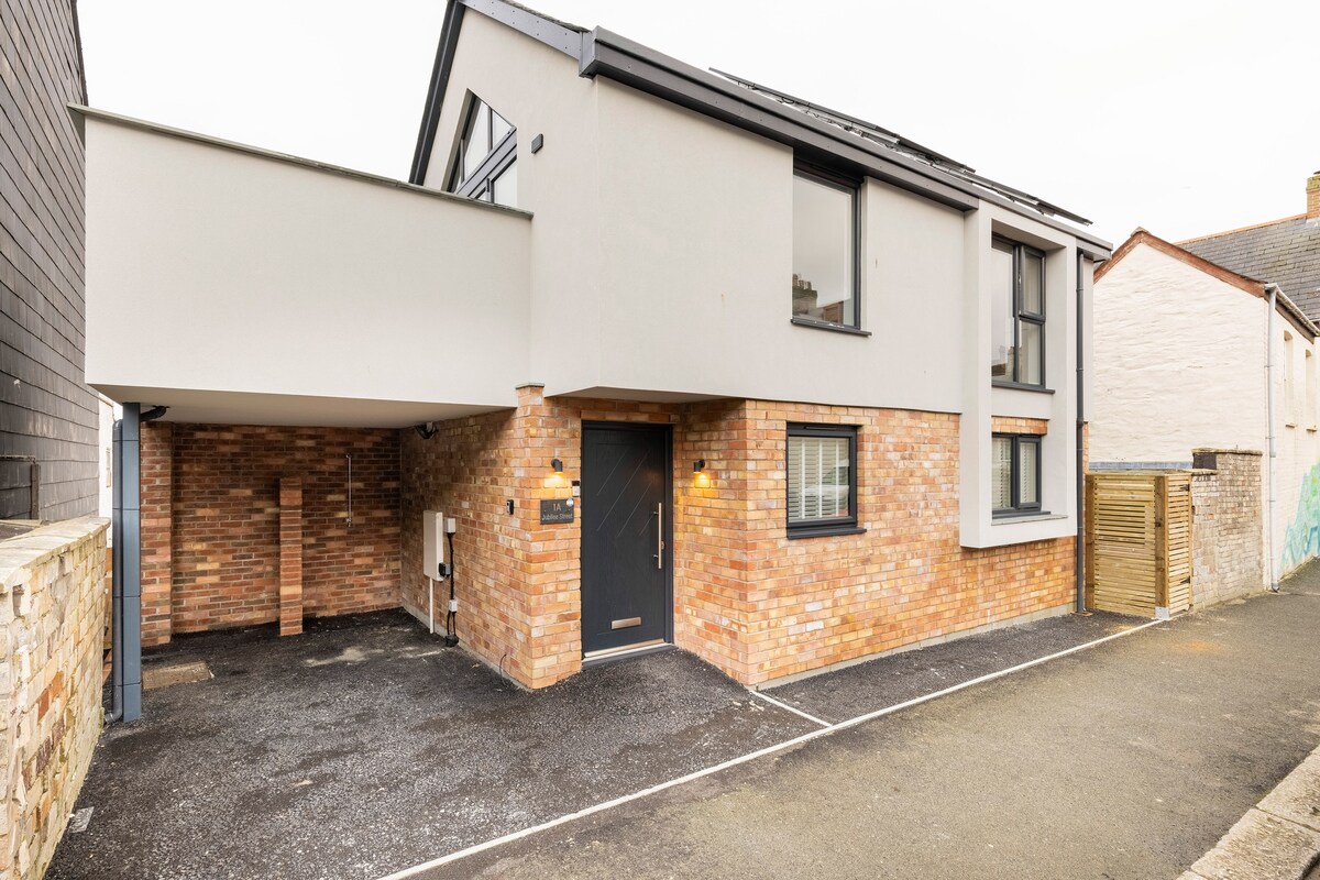 A modern building features a combination of brick and smooth exterior walls. A covered entryway is positioned at the front, with exterior lighting illuminating the entrance. Off-street parking is provided in front, allowing for easy access.