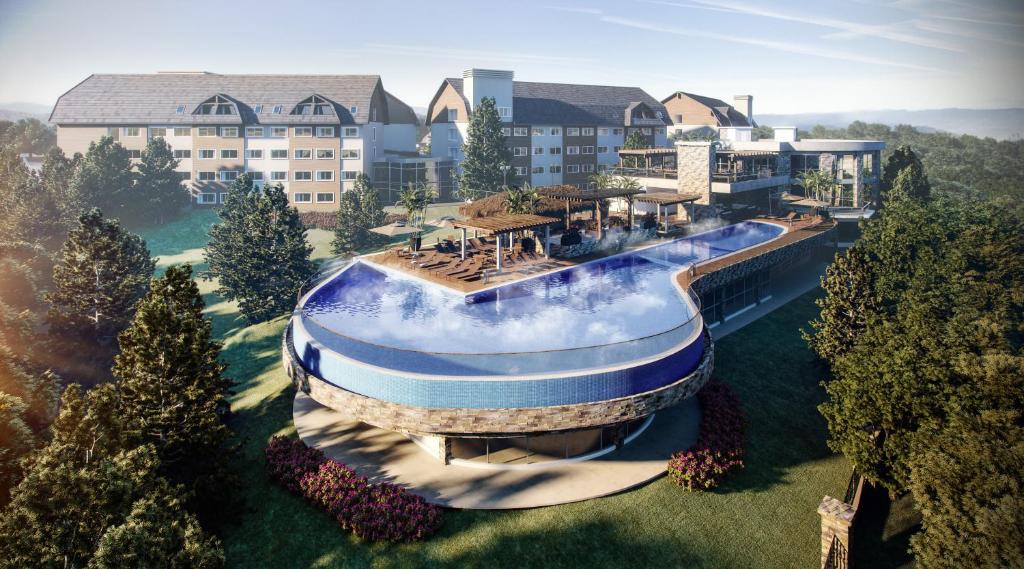 An expansive resort complex is set within lush surroundings, featuring a unique curvilinear pool that appears to blend with the landscape. Spacious lounge areas with sunbeds and canopies are provided, while the adjoining hotel structure showcases a modern architectural design.