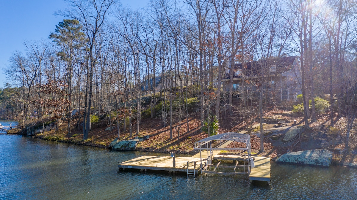 A private dock with a boat lift is positioned along the serene waters of Lake Oconee, surrounded by trees and natural foliage. The gently sloping bank enhances access to the lake, providing a tranquil setting for relaxation or fishing.