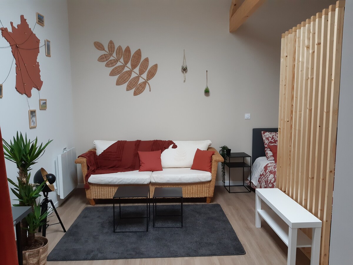 A spacious living area features a comfortable sofa adorned with red and white cushions, framed by a decorative wooden partition. Two black side tables and a white table are placed on a soft rug, while decorative wall elements enhance the room's relaxing ambiance.