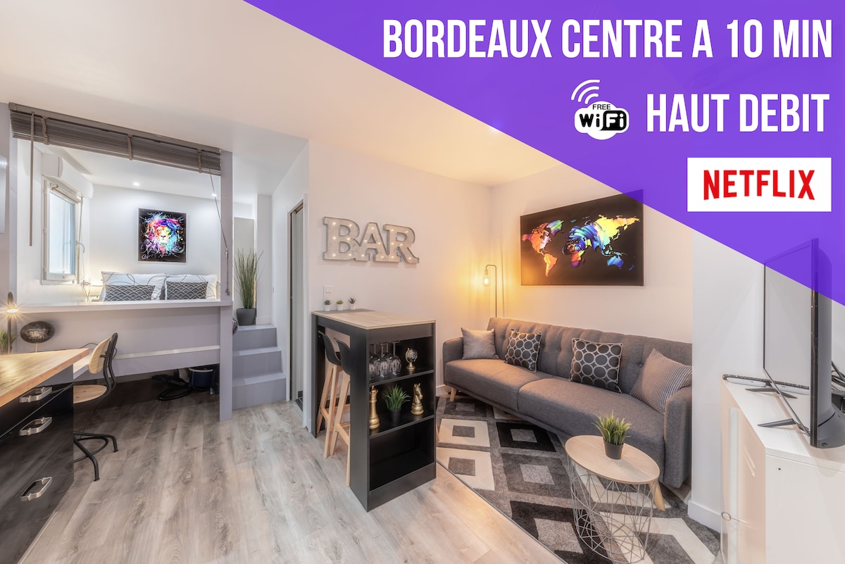 An inviting living area is presented, featuring a comfortable sofa and a stylish bar area. Natural light floods through large windows, while a flat-screen TV is positioned nearby. The modern design is complemented by a workspace with a desk, enhancing the room's functionality.