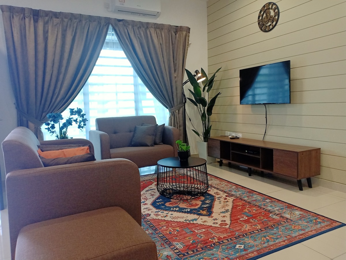 A comfortable living area features a pair of upholstered sofas paired with a round coffee table. A flat-screen TV is mounted on a wooden stand, while a textured rug adds warmth to the tiled floor. Natural light filters through sheer curtains, and indoor plants provide a fresh touch.