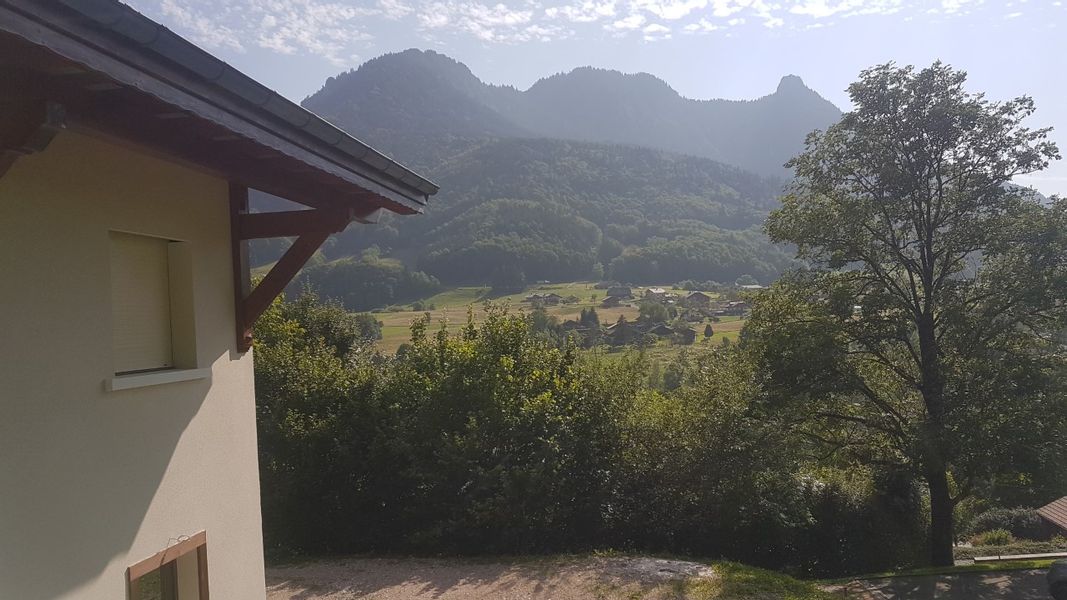 A serene mountain view is displayed, featuring rolling hills and lush greenery. The sunlight gently illuminates the landscape, providing a sense of tranquility. A portion of the building's exterior is visible in the foreground, blending with the natural surroundings.