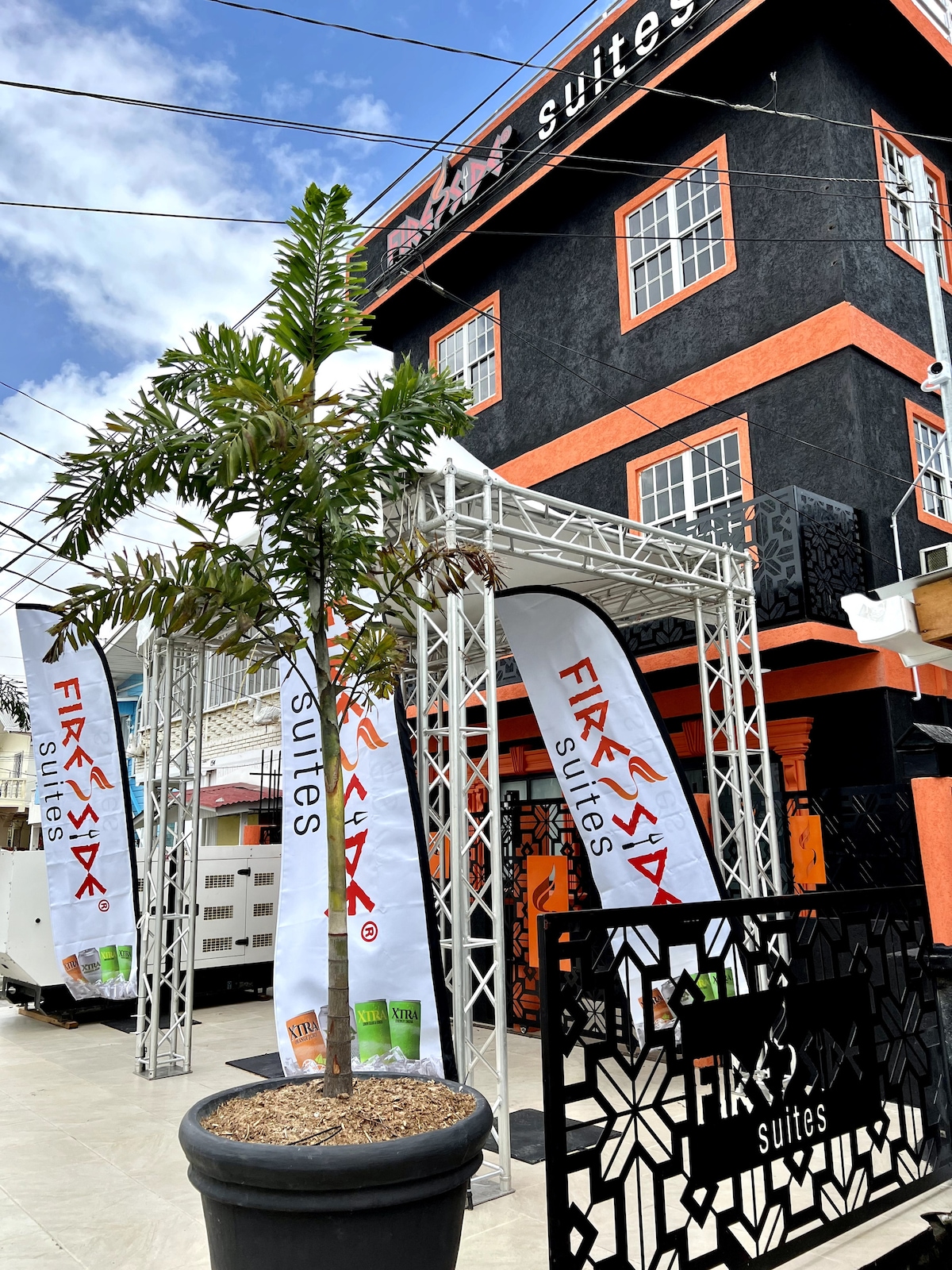 The exterior of the building showcases a modern design with vibrant colors, featuring a prominent entrance flanked by decorative flags. A potted palm tree adds a touch of greenery, and the structured signage is clearly visible, providing identification for the property.