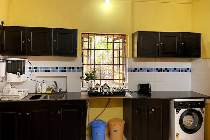 Fully equipped kitchen with a cooking gas, washing machine, water filter, fridge, microwave, toaster, mixer/blender, kettle, cooker, cooking pots/pans, essential dishes, plates, and other crockery.