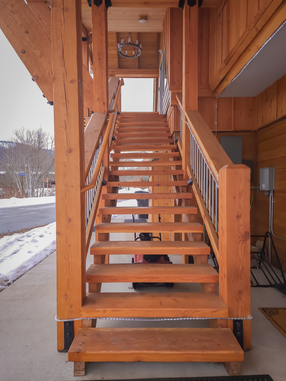 A wooden staircase made of warm-toned planks leads upward. The steps are bordered by railings and are situated outside the unit. Snow is visible on the ground, suggesting a winter setting. The entrance to the building is positioned above the staircase.