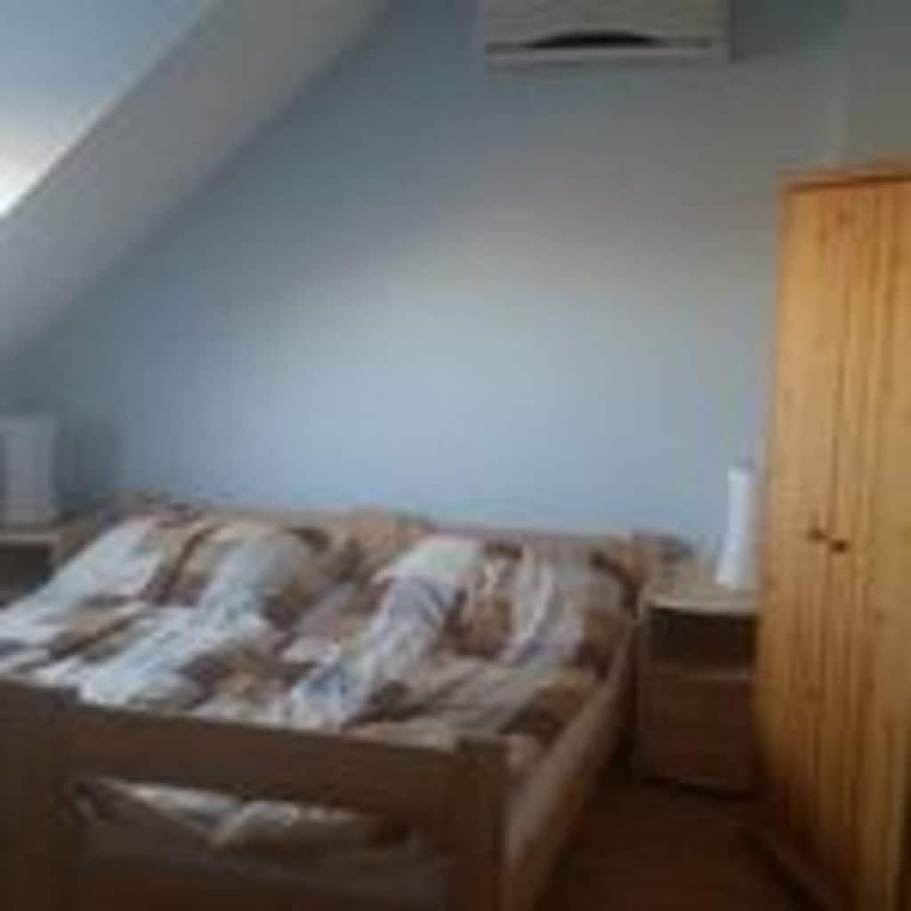 An air-conditioned sleeping area features a spacious bed with a striped comforter. Natural light flows in from a window, illuminating the soft blue walls. A wooden wardrobe and a bedside table are positioned nearby, providing functional storage and surface space.