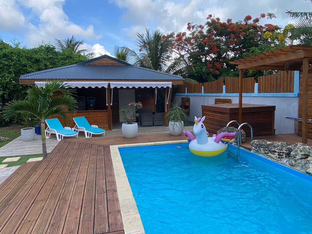 A relaxing outdoor space is highlighted by a turquoise pool, featuring a colorful unicorn float. Comfortable lounge chairs and a wooden deck surround the pool, while a shaded gazebo and potted plants provide a welcoming atmosphere. Lush greenery creates a serene setting.