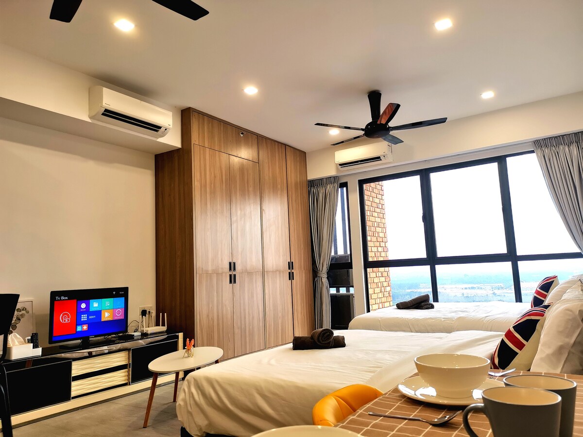 The spacious bedroom features two wide beds with neutral-toned bedding, complemented by decorative pillows. A flat-screen TV is positioned on a modern media console. Panoramic windows allow natural light to fill the room, while a sleek wooden wardrobe adds storage options.