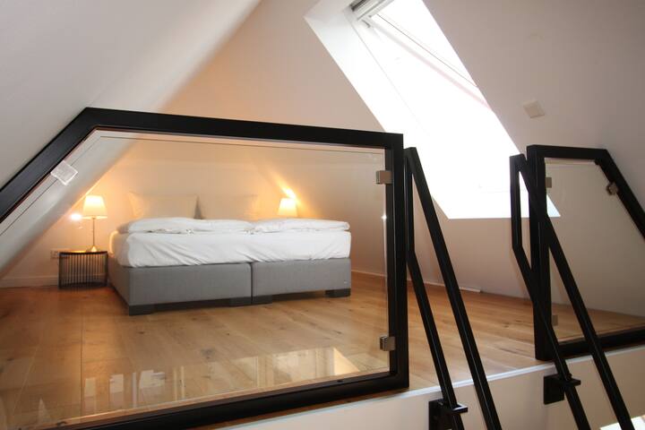 Schlafkoje: Galerie mit einem hochwertigen Boxspringbett aus deutscher Herstellung. Blick aus dem Fenster zum Seekanal mit ein- und ausfahrenden Schiffen.