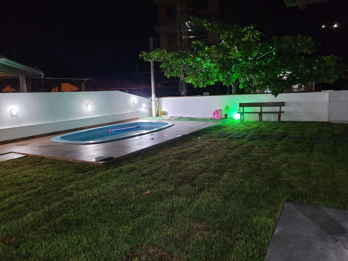 A well-maintained outdoor space is illuminated at night, featuring a circular pool surrounded by a wooden deck. A manicured lawn with low lighting enhances the atmosphere, while a wooden bench is positioned nearby, perfect for quiet relaxation.