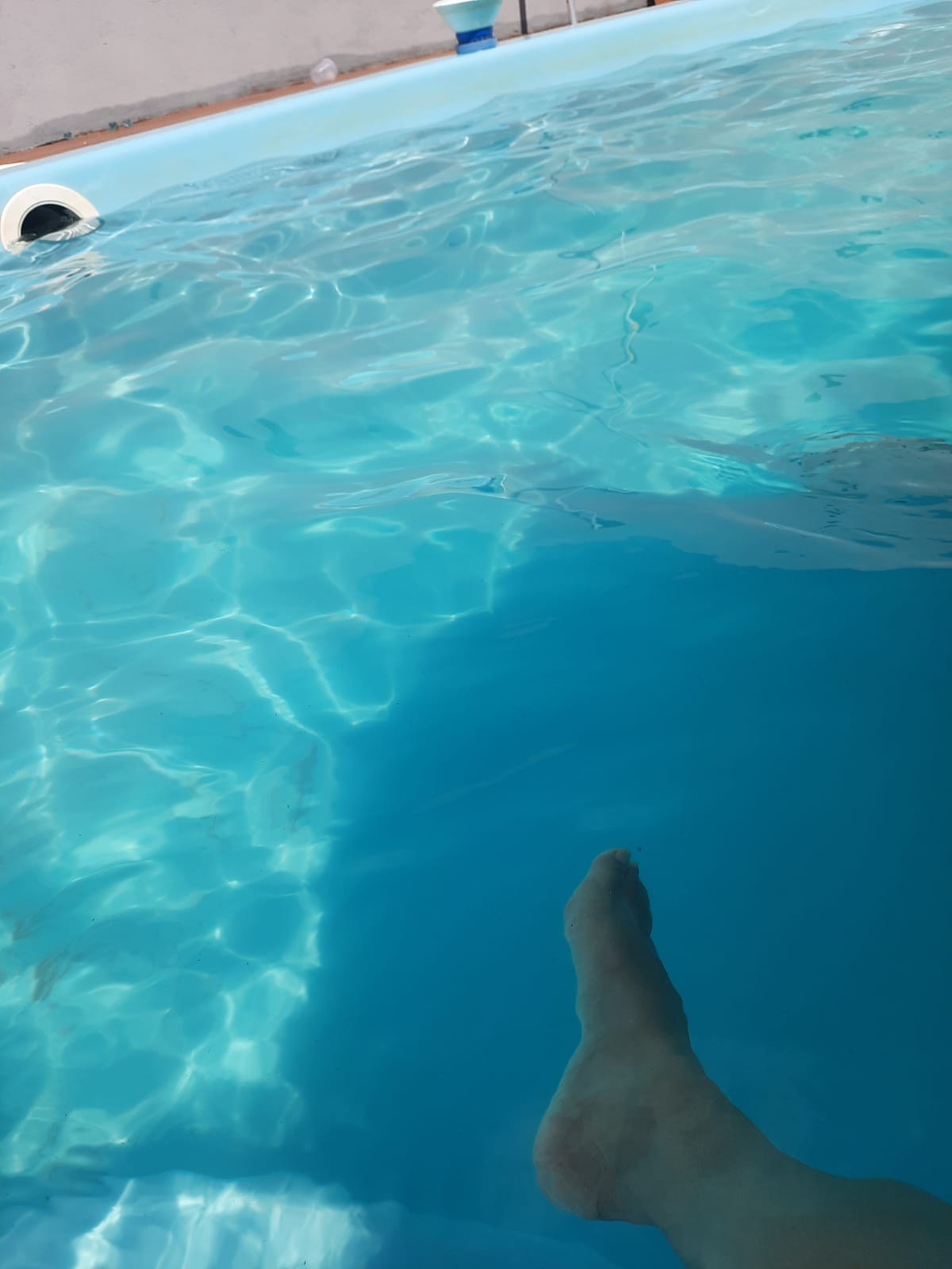 The image captures a close-up view of a person’s foot submerged in a clear, turquoise pool. Gentle ripples in the water reflect light, creating a serene and inviting atmosphere.