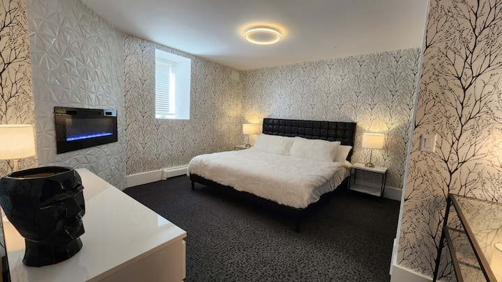 White Trees, el dormitorio junto al Onyx Lounge. Cama tamaño king con ropa de cama de piel sintética ridículamente suave. Pared decorativa con azulejos personalizada con chimenea. Armario doble grande y cómoda completa de 6 cajones para todas las necesidades de tu estancia larga.