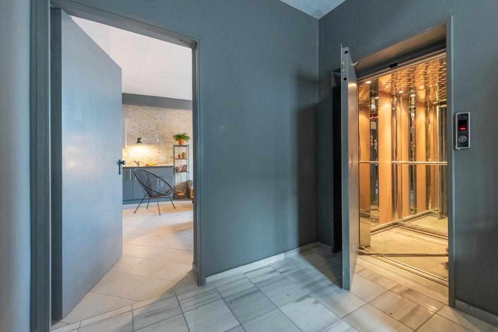 An elevator is seen on the right, its doors open to reveal a mirrored interior. To the left, an open doorway leads into a modern studio space with subtle decor elements. The flooring is tiled, creating a sleek, polished appearance.