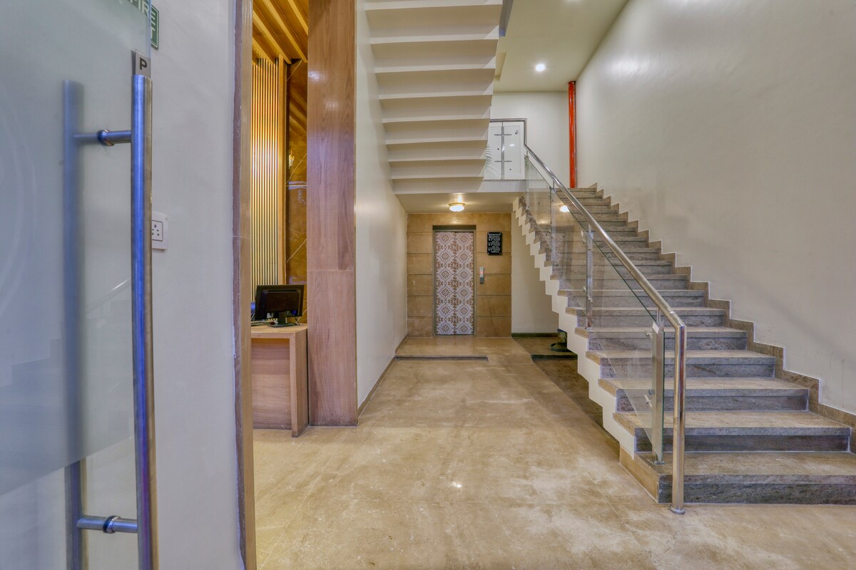 A spacious entrance area is featured, showcasing polished stone tiles. A modern staircase with stainless steel railings leads to upper levels. An elevator door is visible, alongside a reception desk located to the left, enhancing accessibility.