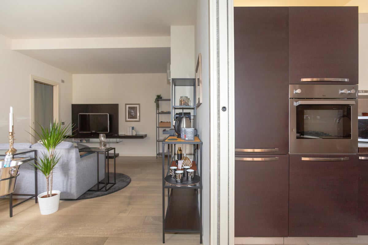 A spacious living area is visible, featuring a comfortable sofa, wall-mounted television, and decorative elements. The adjacent kitchen area displays modern cabinetry and built-in appliances, enhancing functionality. A potted plant adds a fresh touch to the overall design.